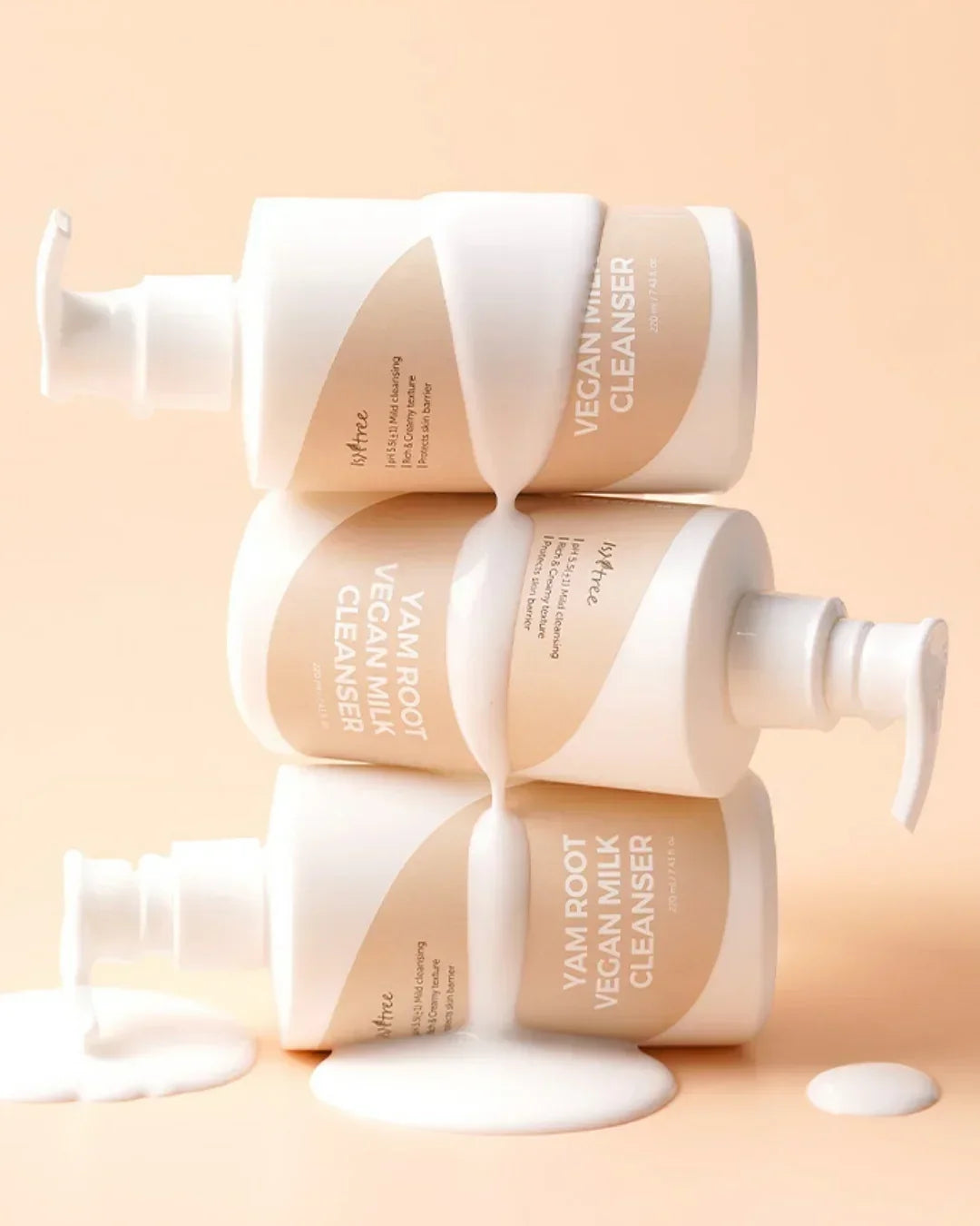 Three stacked bottles of Isntree Yam Root Vegan Milk Cleanser with cream flowing down on peach background