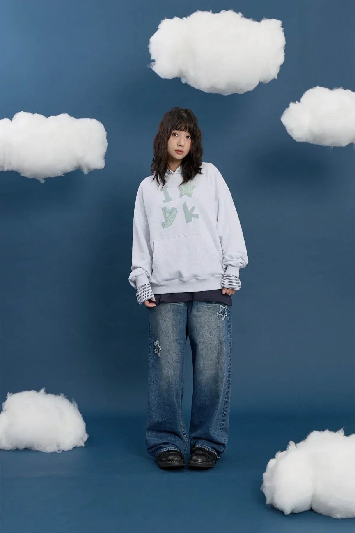 Model in oversized melange white hoodie and wide-leg jeans with applique, blue backdrop, clouds, Korean fashion