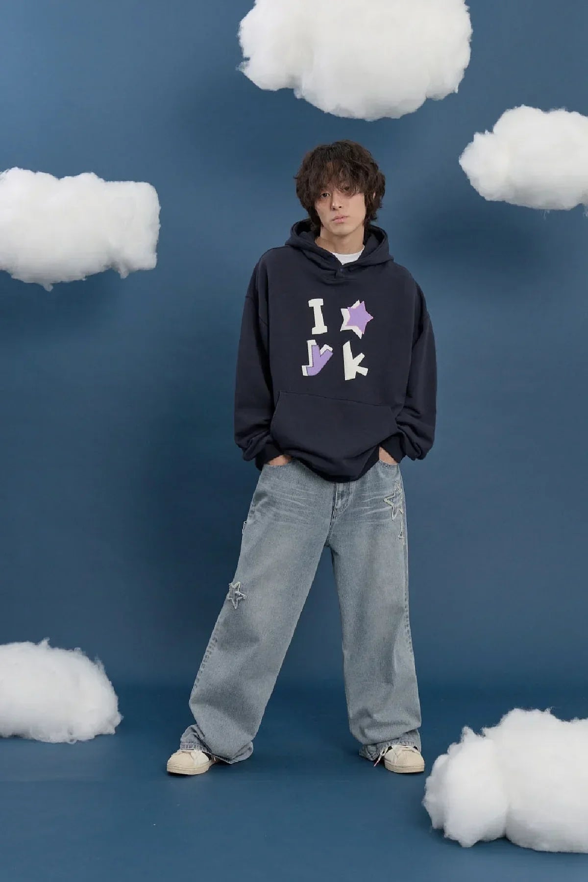 Model wearing navy Korean style hoodie with applique lettering and star, wide-leg jeans, clouds backdrop on Malkn
