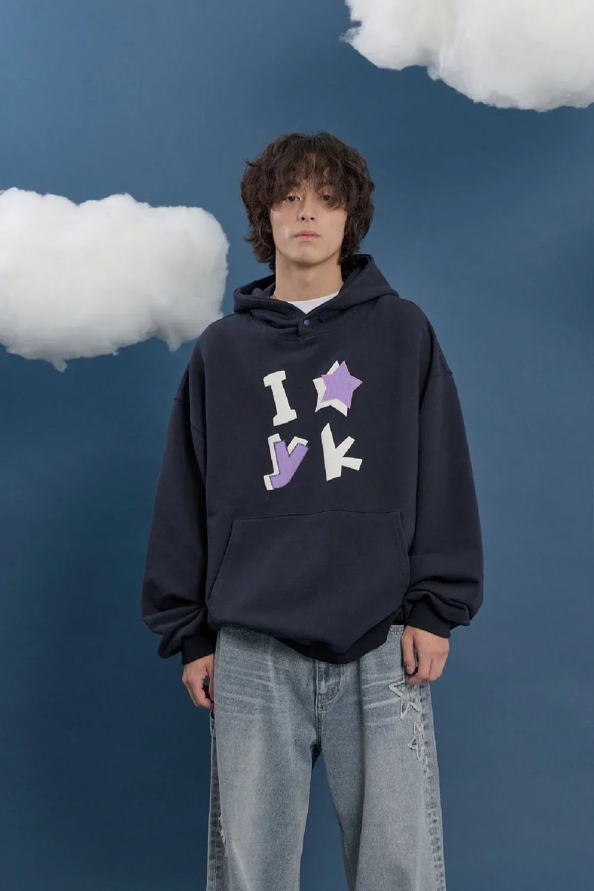 Model in navy Korean fashion hoodie with pastel star applique, light jeans, blue background, Malkn