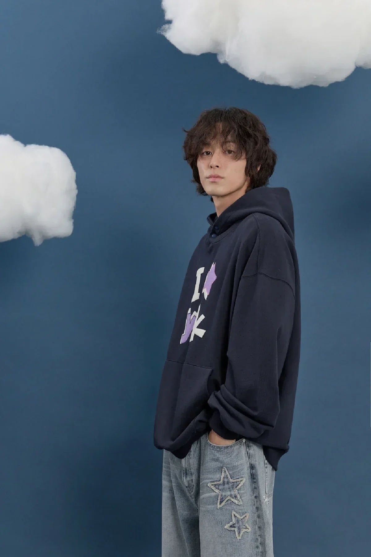 Male model in navy Korean hoodie and star jeans on blue background with cloud props, Malkn fashion