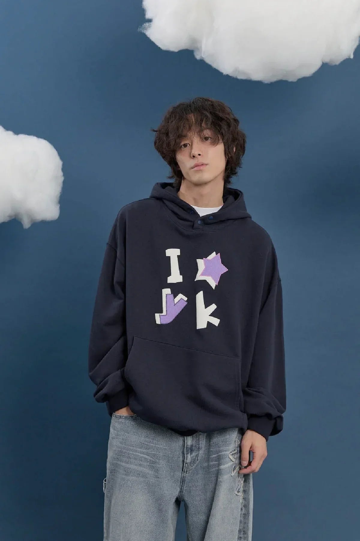 Model in navy hoodie with applique designs, relaxed jeans, Korean fashion, blue studio background