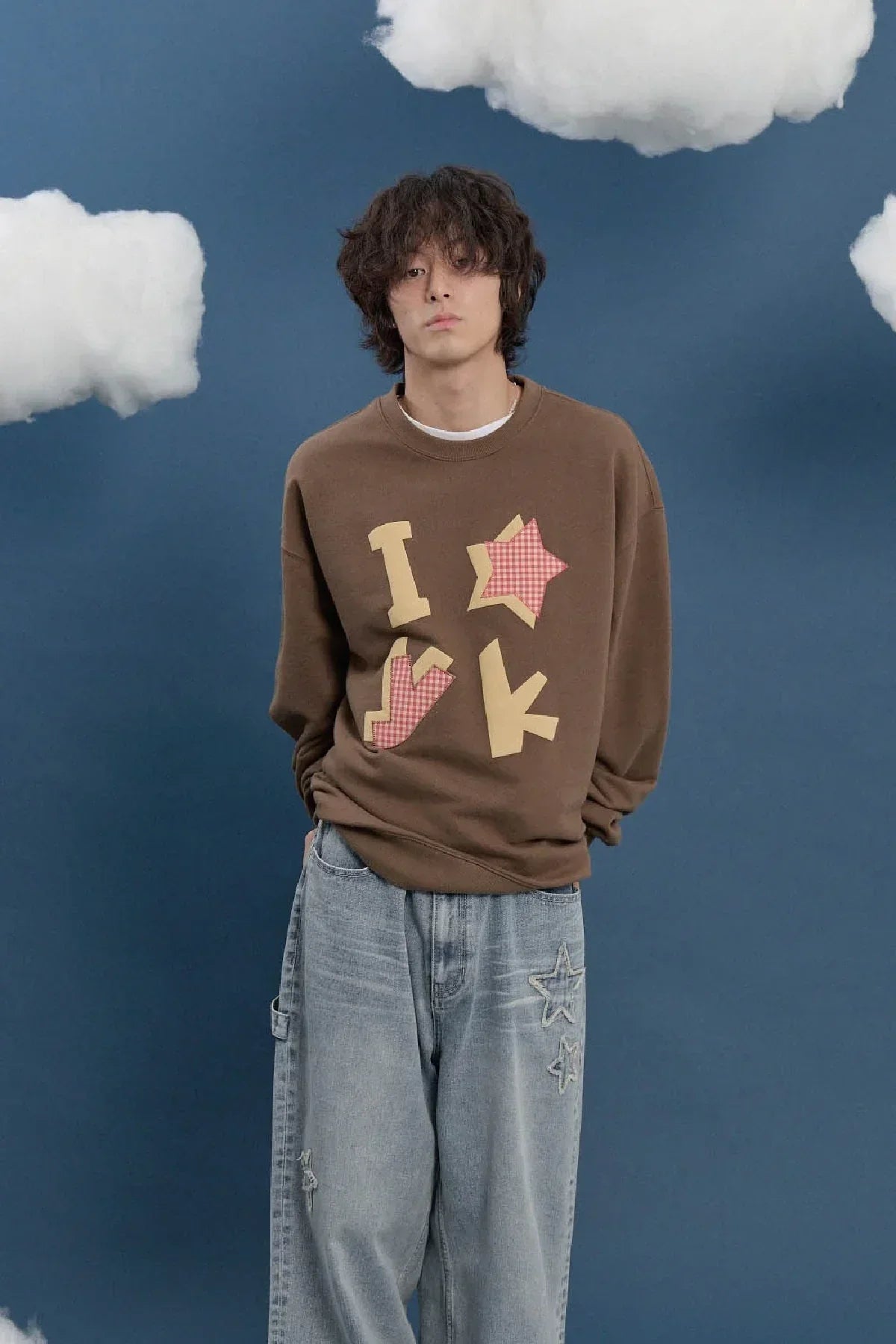 Model in brown Korean applique sweatshirt and baggy jeans, Malkn fashion shoot with cloud props