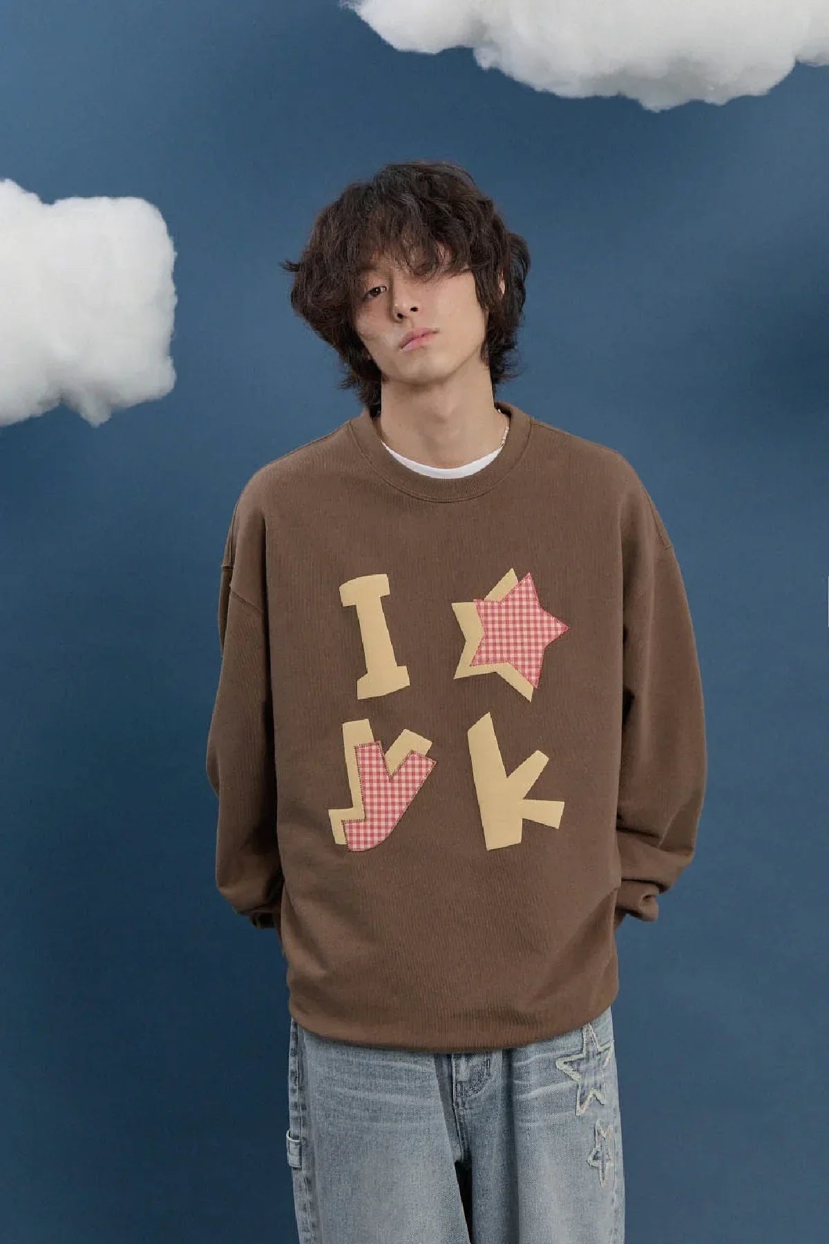Male model wearing brown YK check applique sweatshirt, blue jeans, studio clouds backdrop, Korean fashion on Malkn.