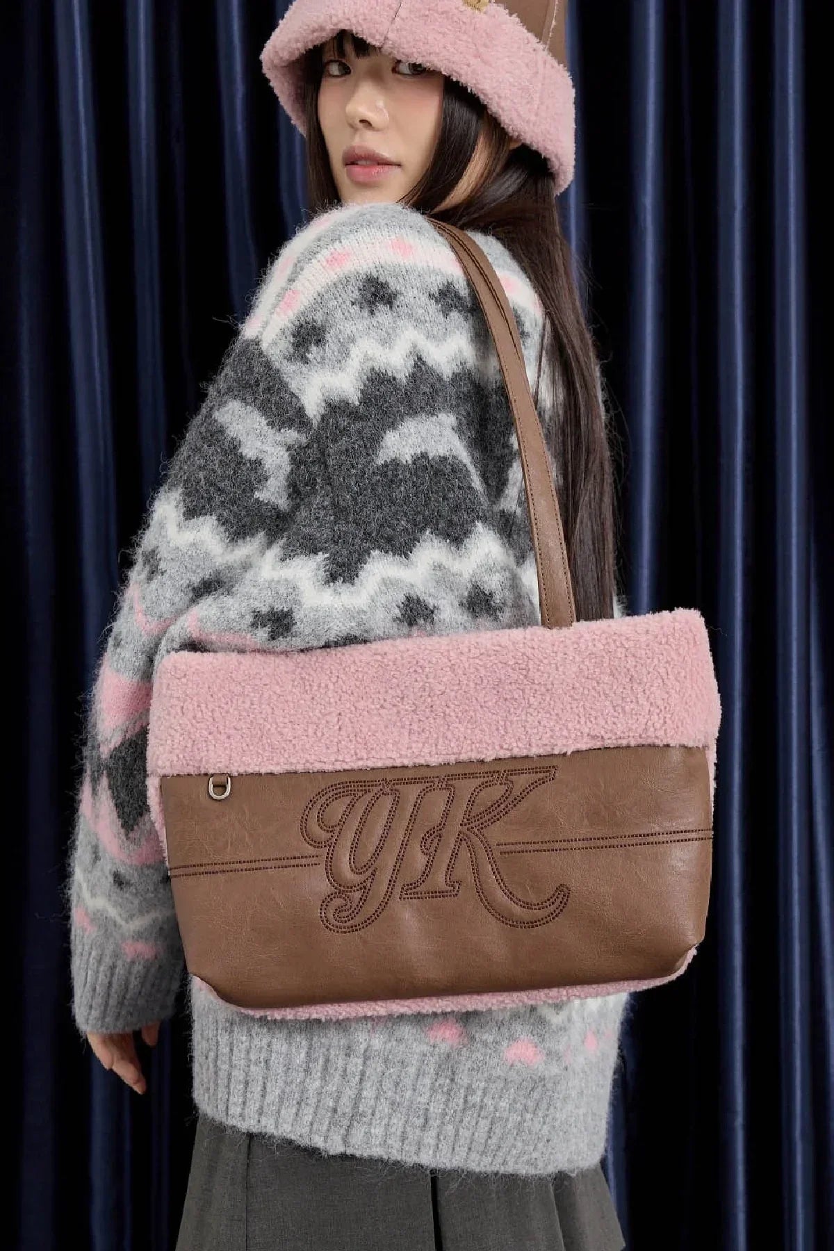 Brown leather and pink shearling shoulder bag with YK logo worn by woman in gray patterned sweater