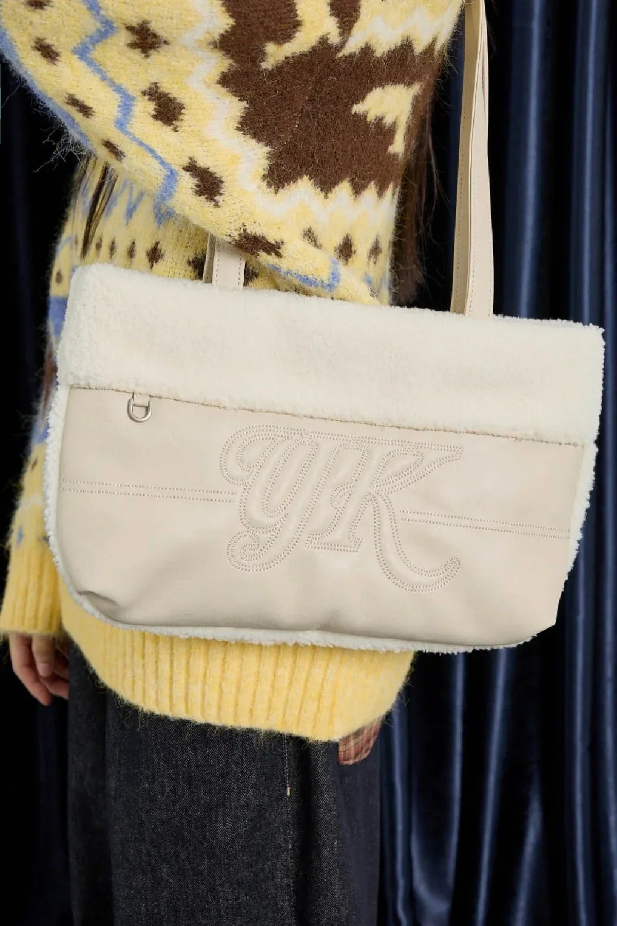 Ivory YK branded shoulder bag with shearling trim worn over yellow patterned sweater and dark jeans