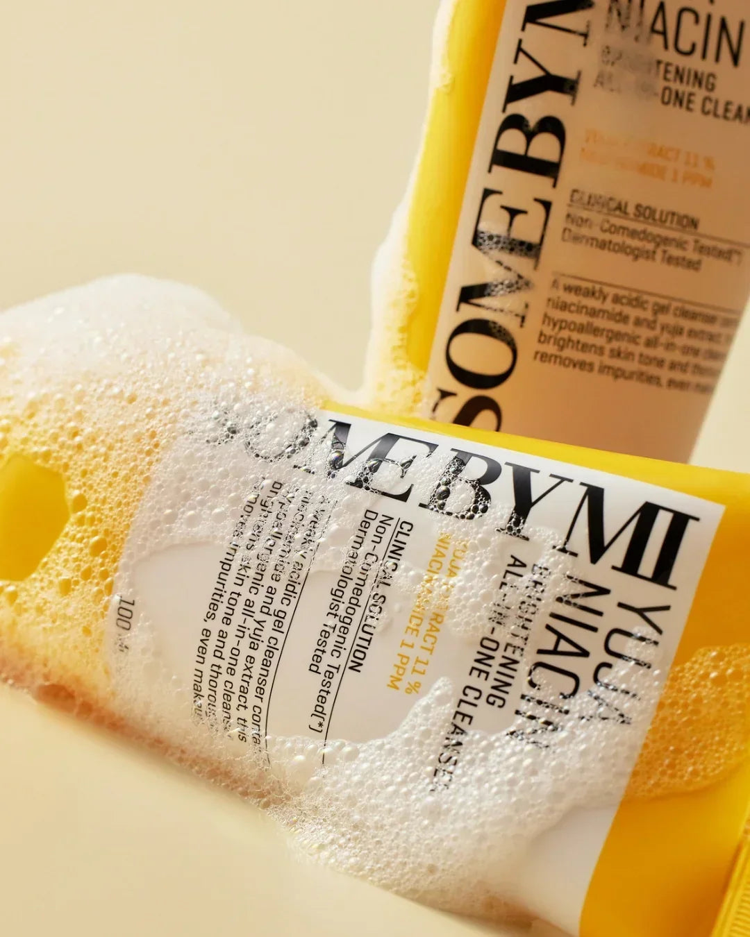 Yuja Niacine Brightening All-in-One Cleanser bottles with foamy bubbles on a beige background