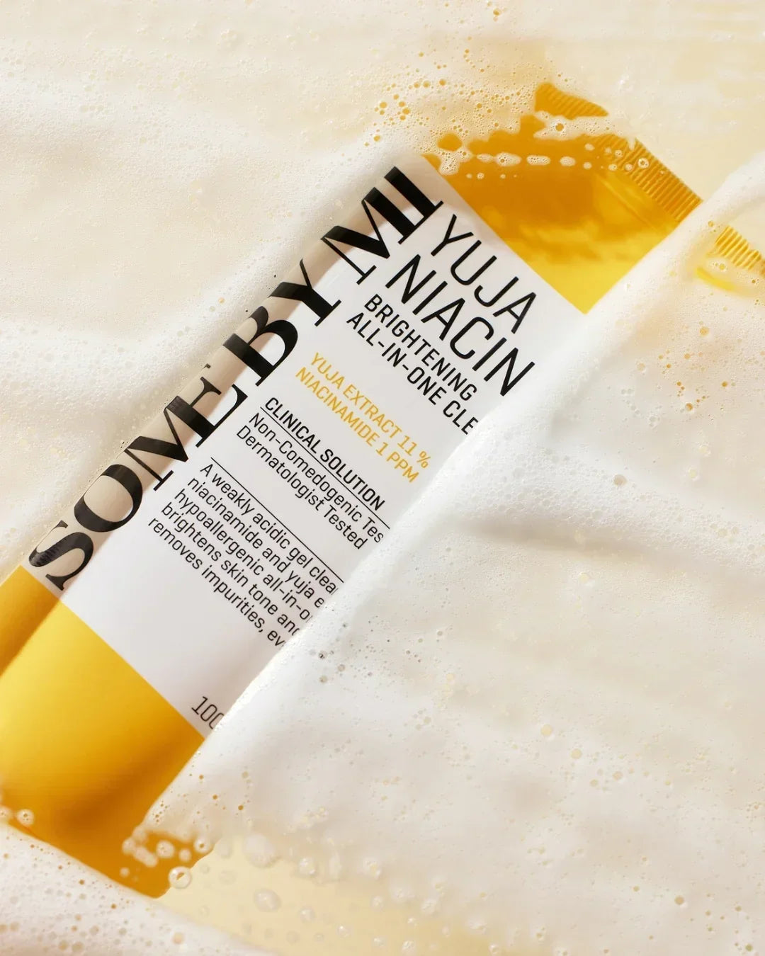 Yuja Niacin Brightening All-In-One Cleanser tube partially submerged in foamy cleanser texture