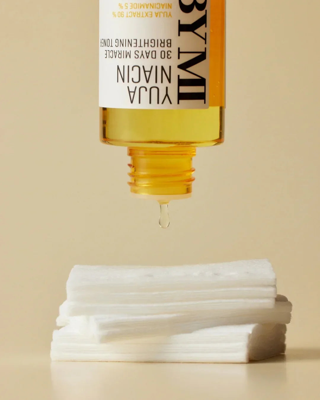 Yuja Niacin 30 Days Miracle Brightening Toner bottle dispensing liquid drop onto white cotton pads