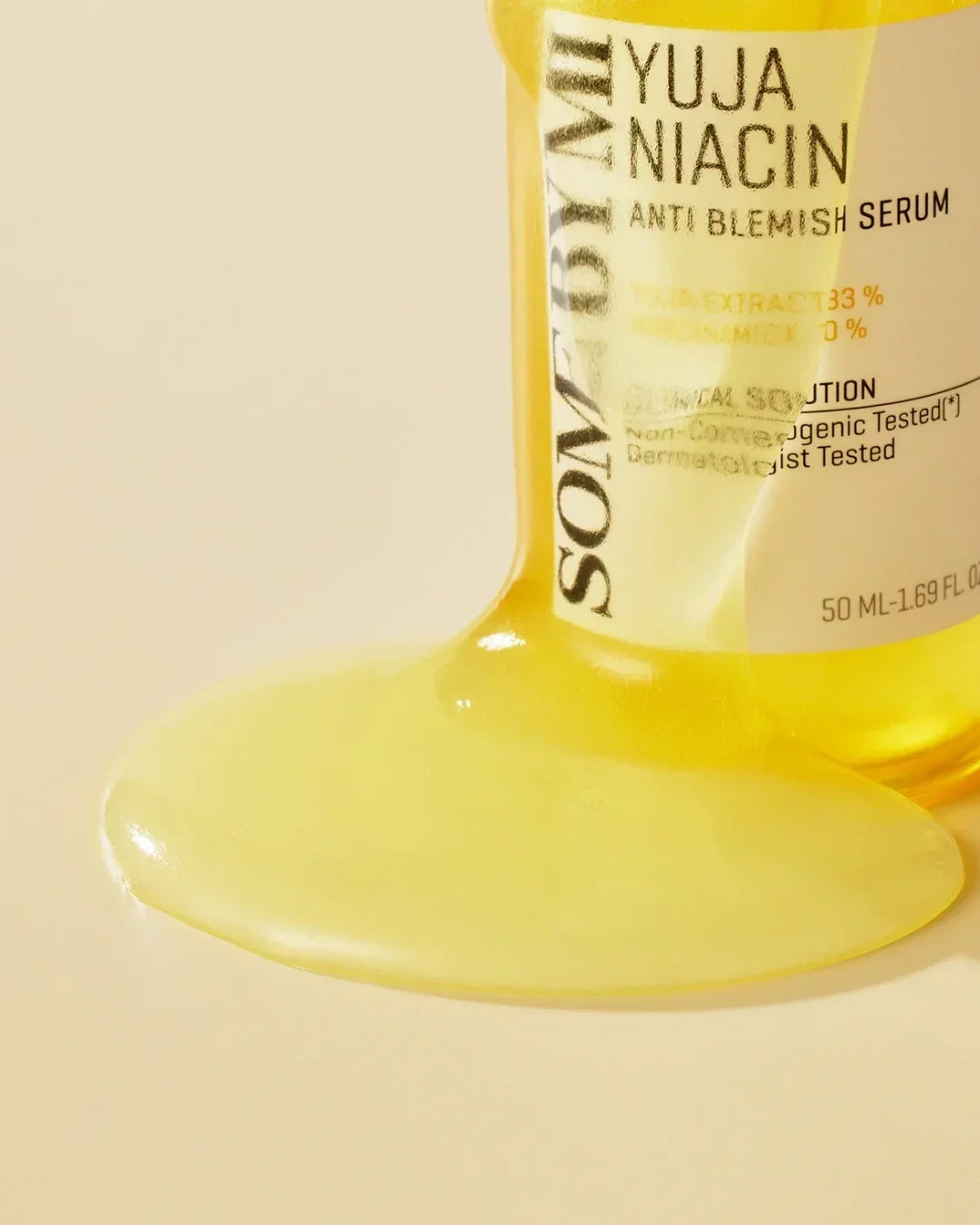 Yuja Niacin anti-blemish serum bottle with spilled yellow serum on beige surface