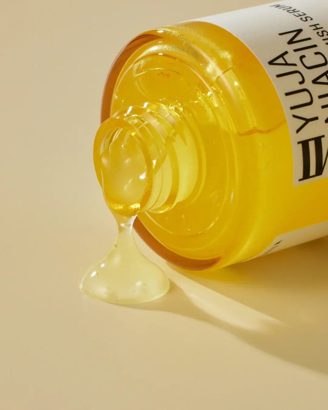 Close-up of Yuja Niacin brightening anti-blemish serum bottle with gel texture on beige surface