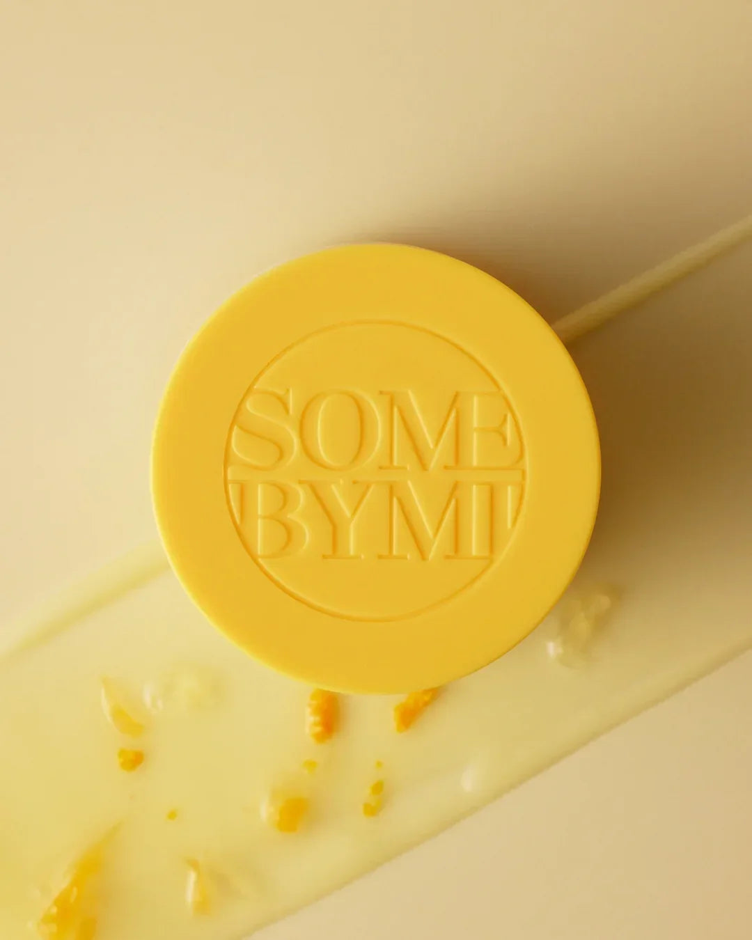 Yellow Some By Mi skincare container on cream background with texture and orange fragments