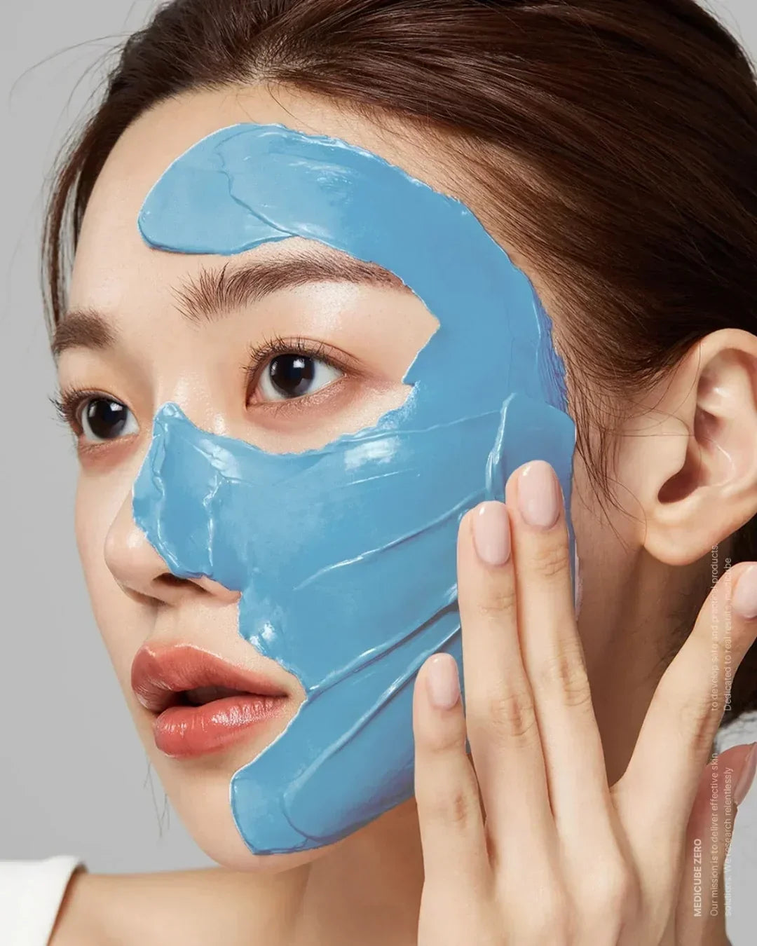 Close-up of woman applying blue blackhead mud mask on face with fingers, clear skin care routine