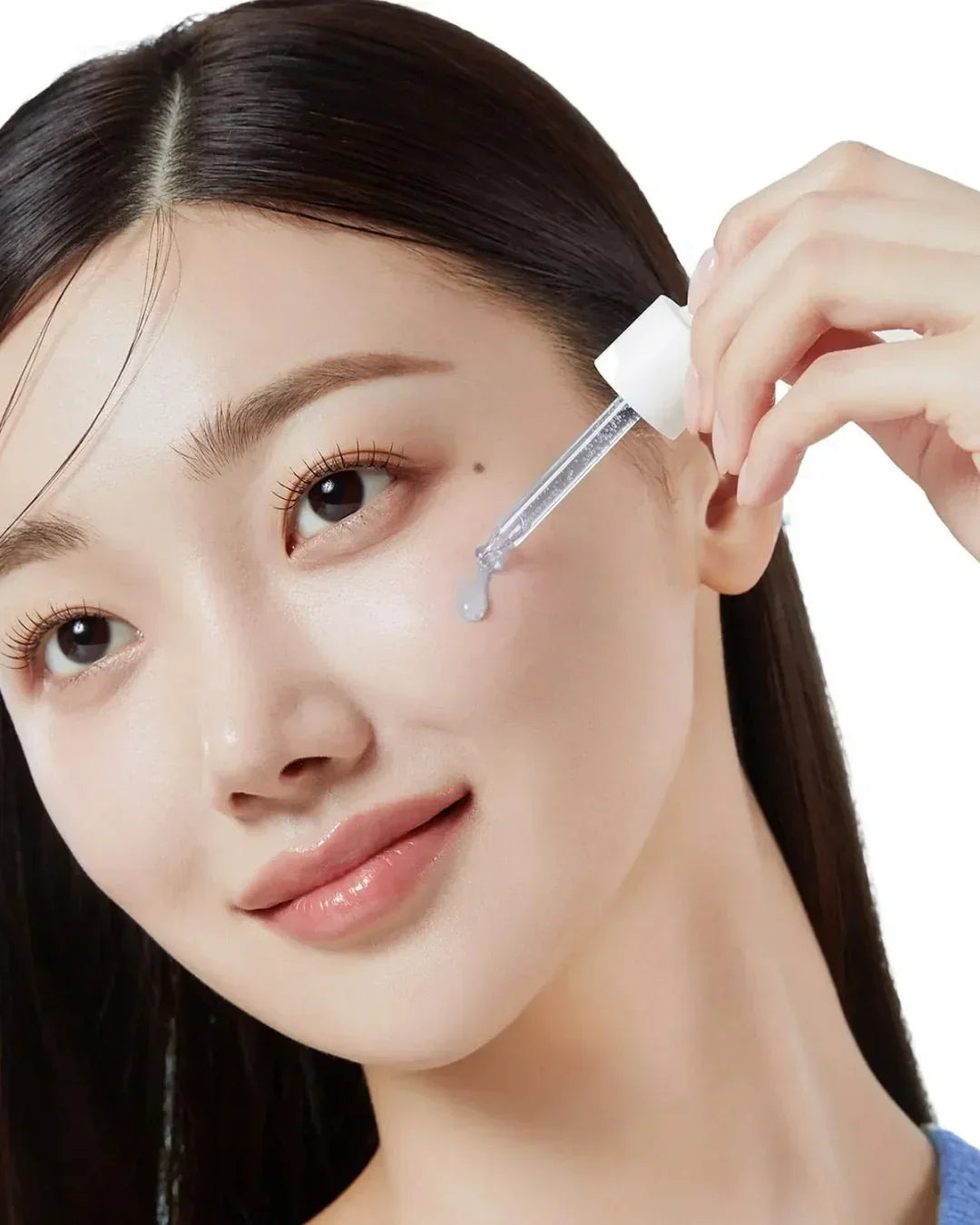 Close-up of woman applying clear skincare serum to cheek using dropper, smooth glowing skin