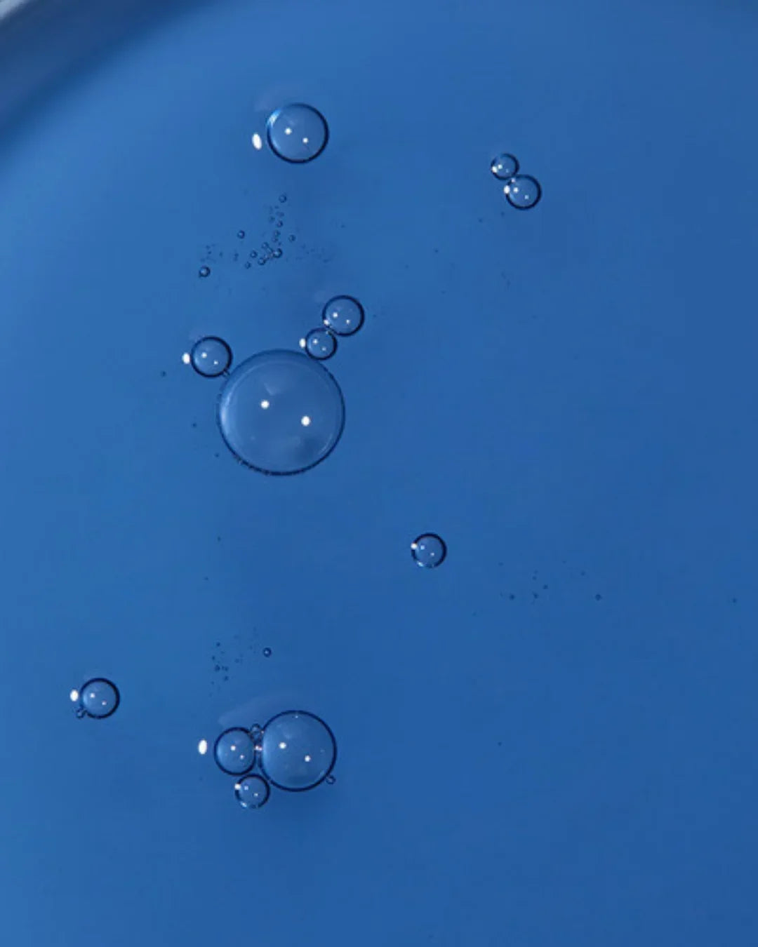Close-up of clear serum droplets on blue background showing liquid skincare texture