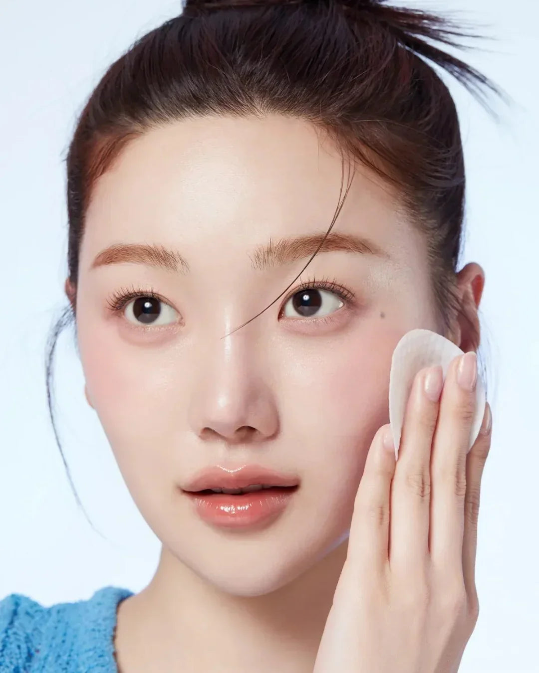 Young woman with clear skin gently applying a white pore pad to her cheek for skincare