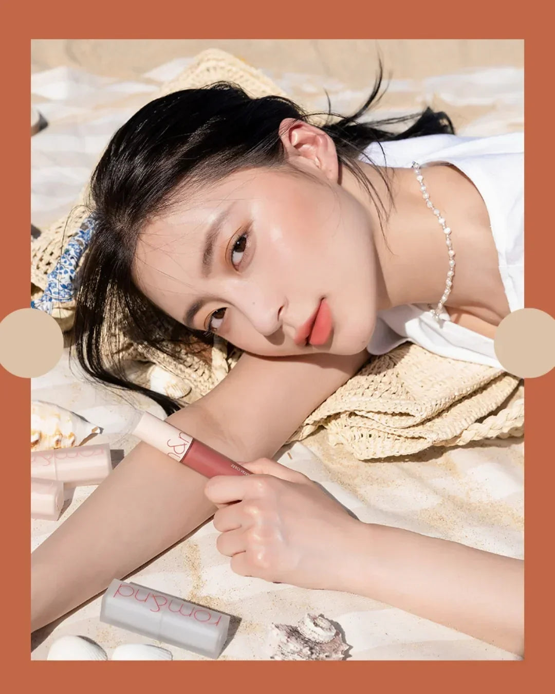 Close-up of woman with natural makeup lying on sandy beach holding pink velvet tint lipstick