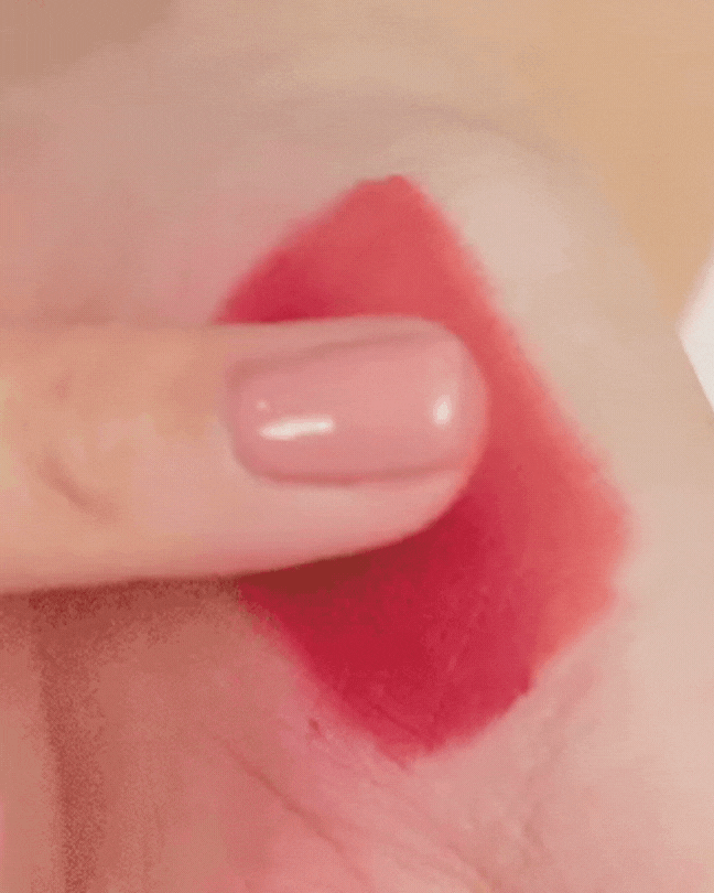 Finger swiping deep red velvet tint lipstick on skin, demonstrating smooth makeup application